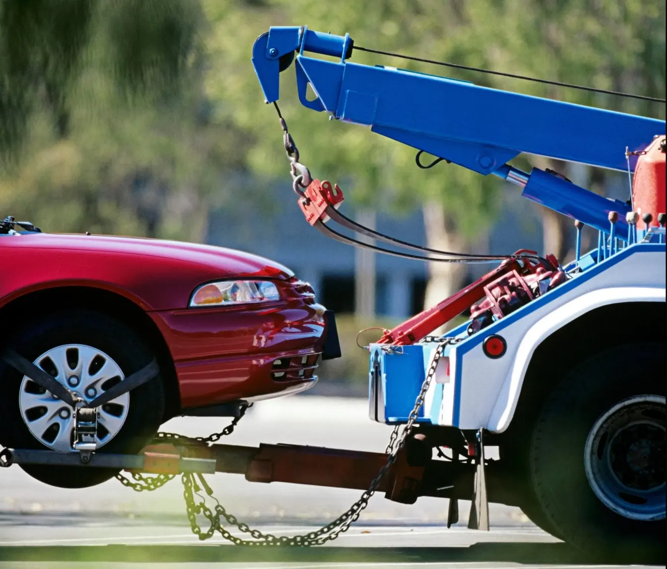 A Tow Truck Lifts A Red Car, Showcasing Its Suspension And The Truck'S Power.